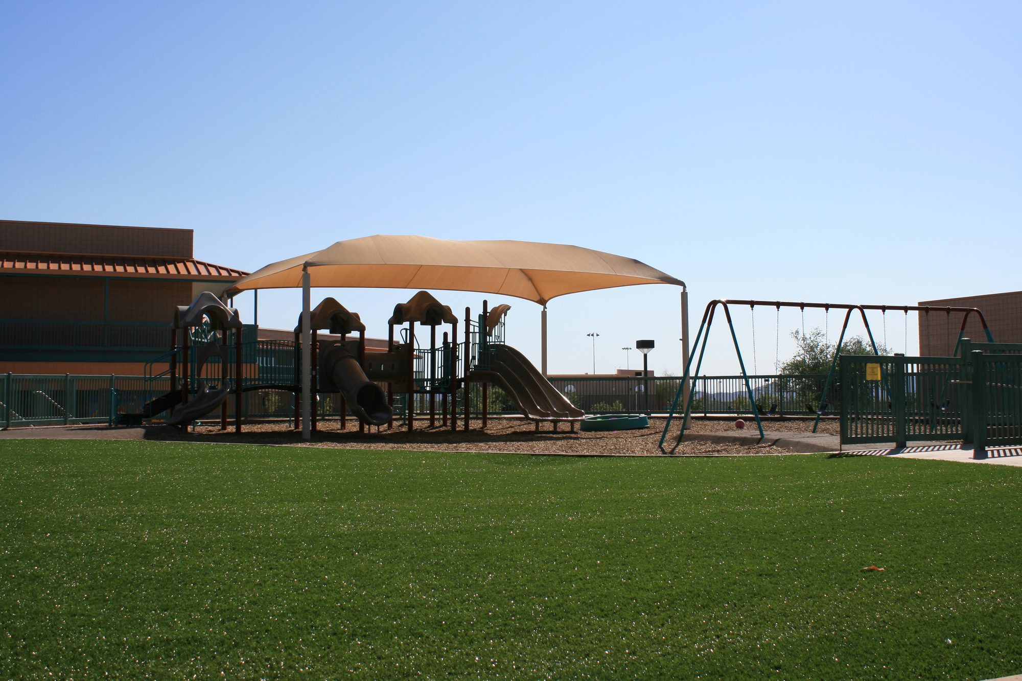 Custom artificial turf playground with shade trees and play features in an Arizona backyard
