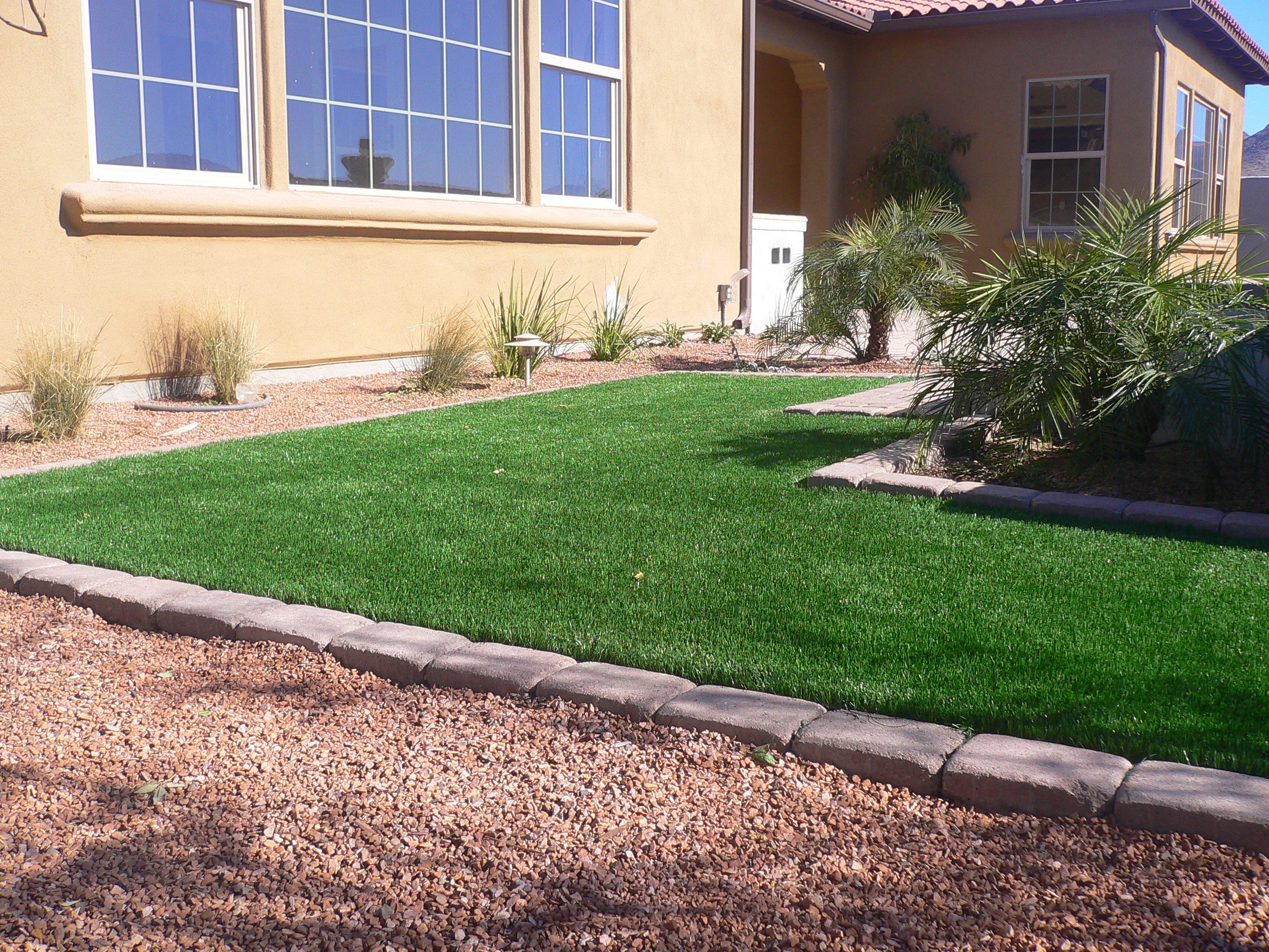 An Arizona front lawn of artificial turf with a large multi pane window wall facing it, the kind of glass elevation that can focus reflected heat onto the surface