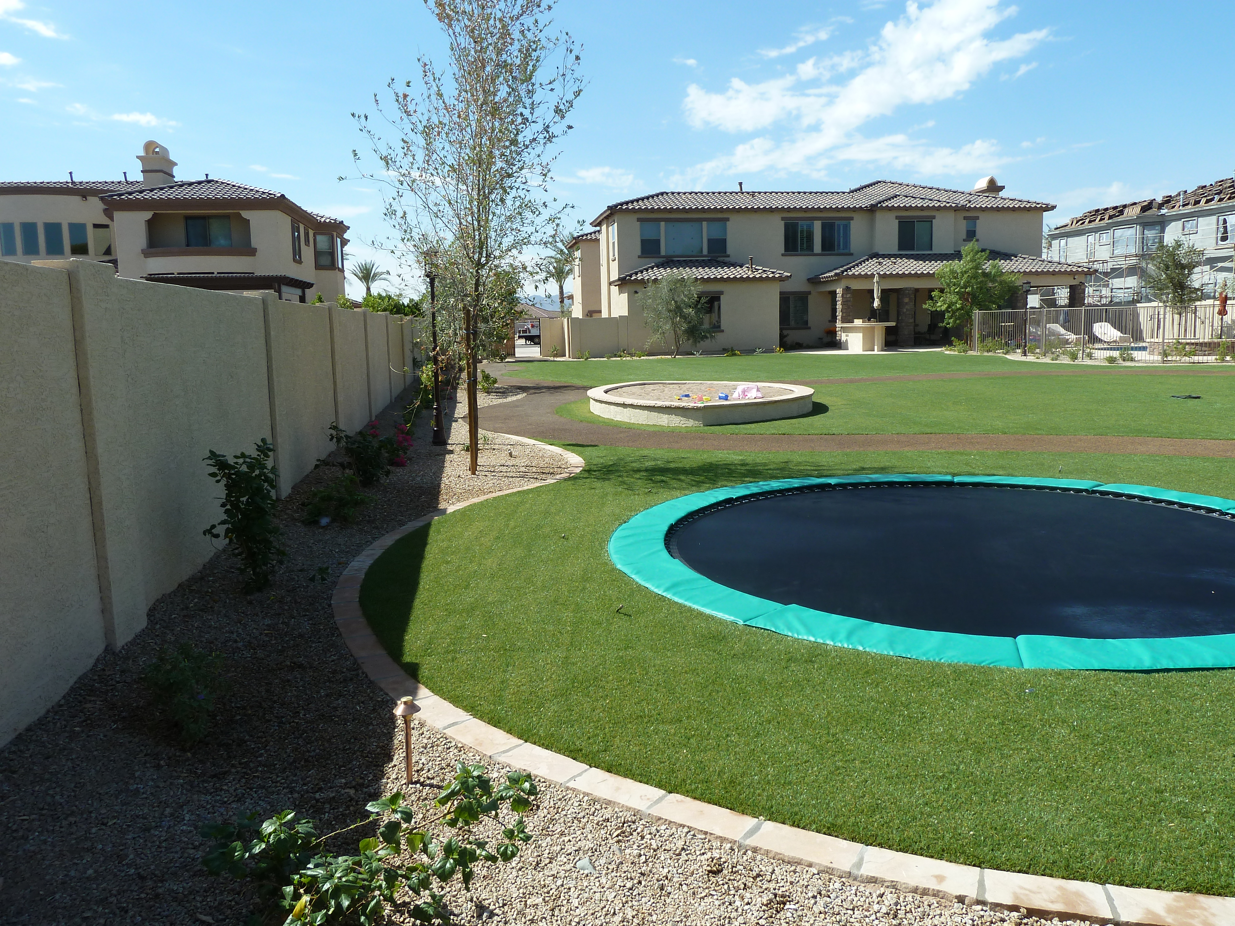 Green in-ground trampoline set flush into artificial turf in an Arizona backyard